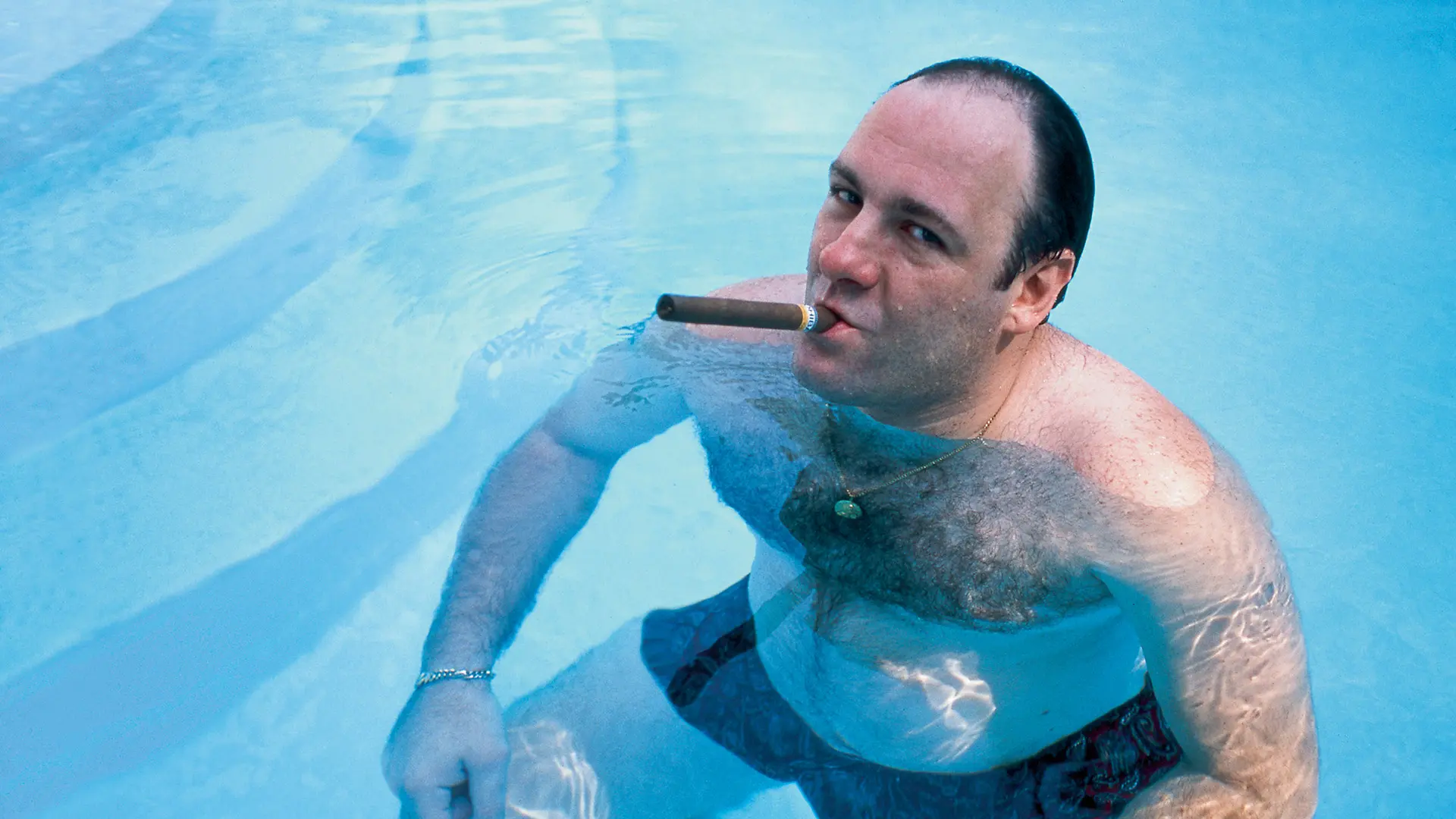 Tony Soprano sumergido en una piscina fumando un puro y mirando con confianza a cámara.