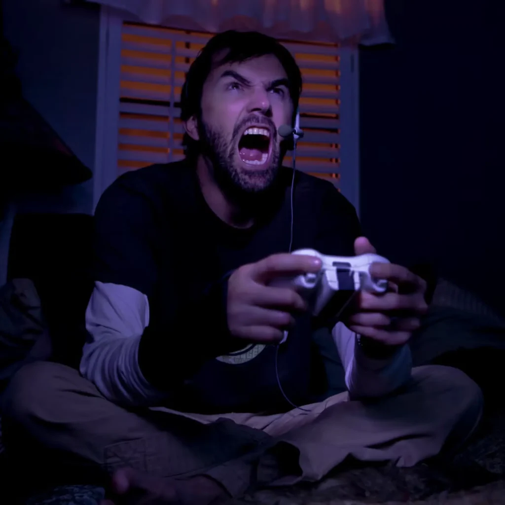 Un jugador adulto grita frustrado frente a una pantalla oscura; la ira es común en las situaciones irritantes en los videojuegos.
