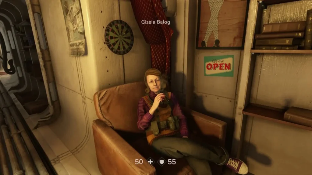 Gizela Balog descansa en un sillón dentro del cuartel aliado, sosteniendo una bebida junto a una diana y carteles viejos.