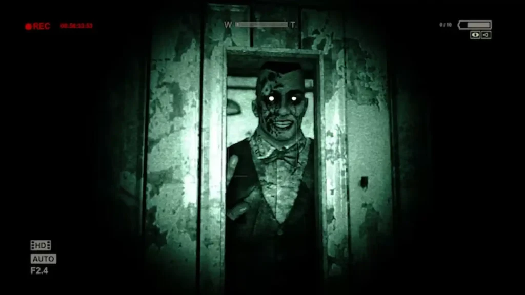 Un asesino sonriente con ojos brillantes aparece ante la cámara de visión nocturna en Outlast, emblema del terror moderno.