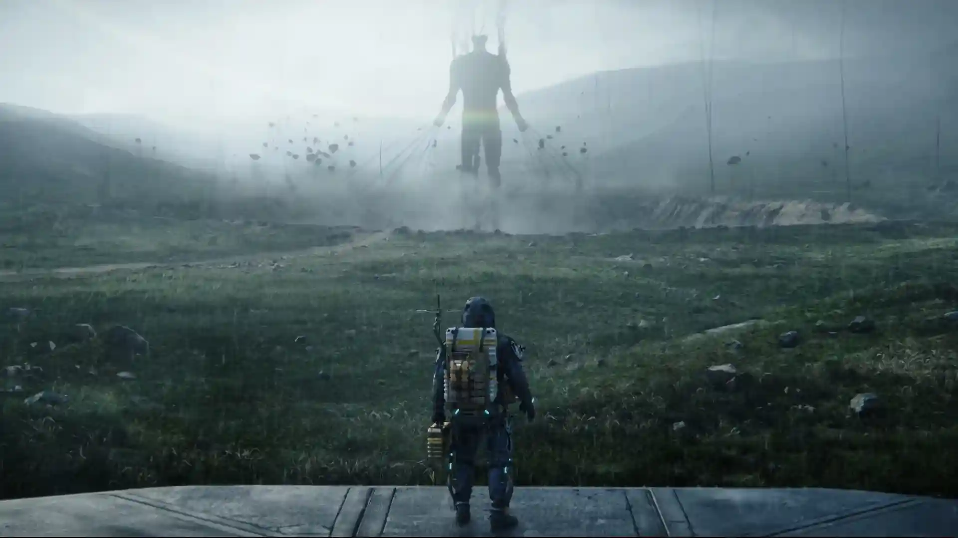 Una entidad fantasmagórica al fondo de un escenario derruido y con niebla, perdido con Death Stranding como el protagonista del videojuego.