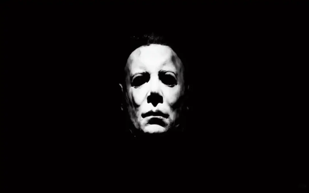 Rostro en sombras de Michael Myers iluminado en blanco, símbolo del terror silencioso de la saga Halloween.