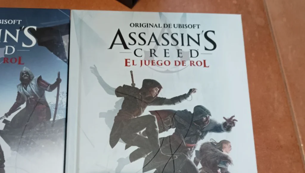 Primer plano de la portada del manual en español que muestra a dos asesinos saltando, parte de las reglas del juego de rol de Assassin's Creed.