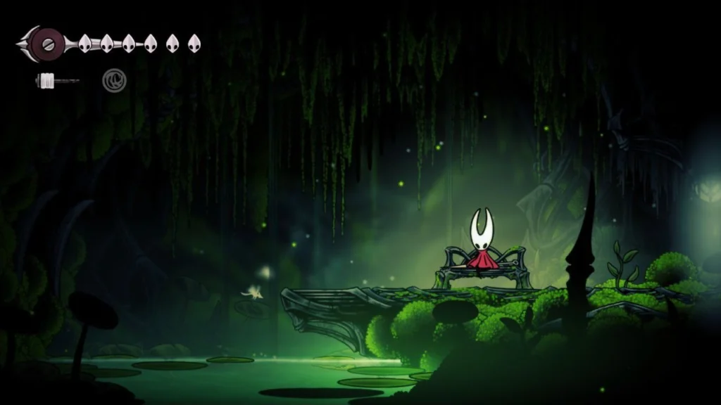 Hornet descansa sentada en un banco de hierro dentro de una caverna llena de musgo y vegetación en Silksong.