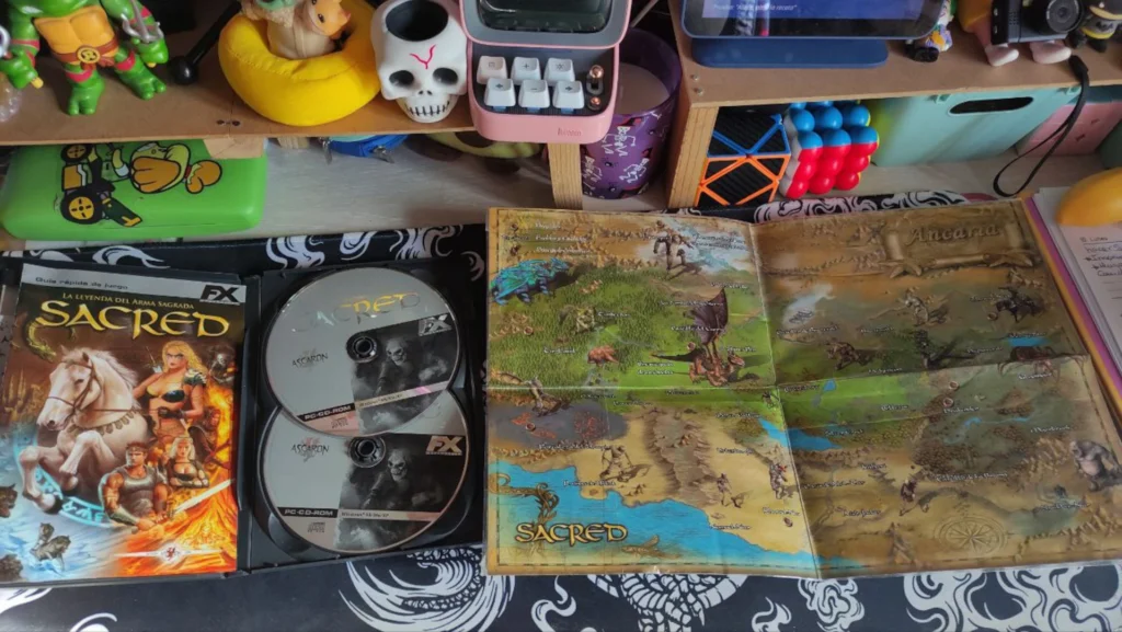 Edición física de Sacred abierta con sus dos discos y el mapa detallado del mundo de Ancaria.