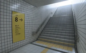 Exit 8: escalera hacia la superficie junto al cartel amarillo de la Salida 8 y su lista de lugares cercanos.