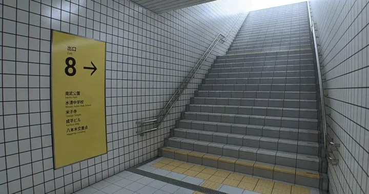 Exit 8: escalera hacia la superficie junto al cartel amarillo de la Salida 8 y su lista de lugares cercanos.